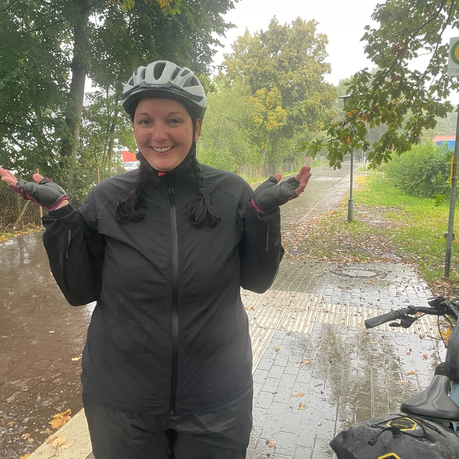 Radfahrerin stellt sich vor starkem Regen unter ein Dach