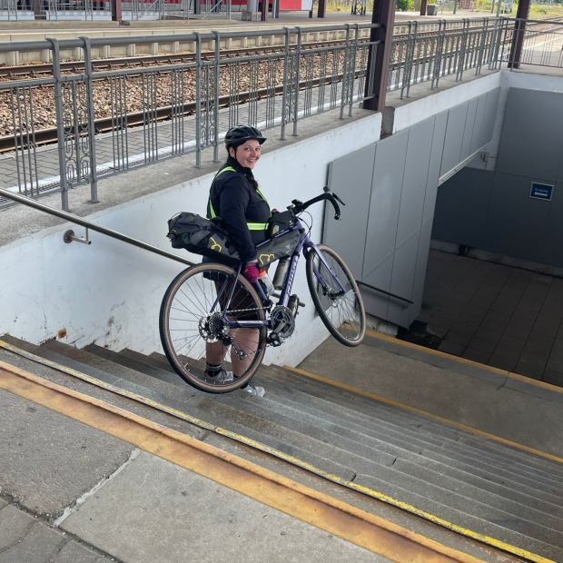 Frau trägt mit Reisetaschen bepacktes Fahrrad eine Bahnhofstreppe runter.