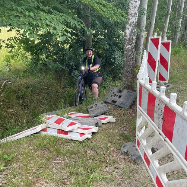 Frau trägt Fahrrad durch Straßengraben an Bauzaun vorbei