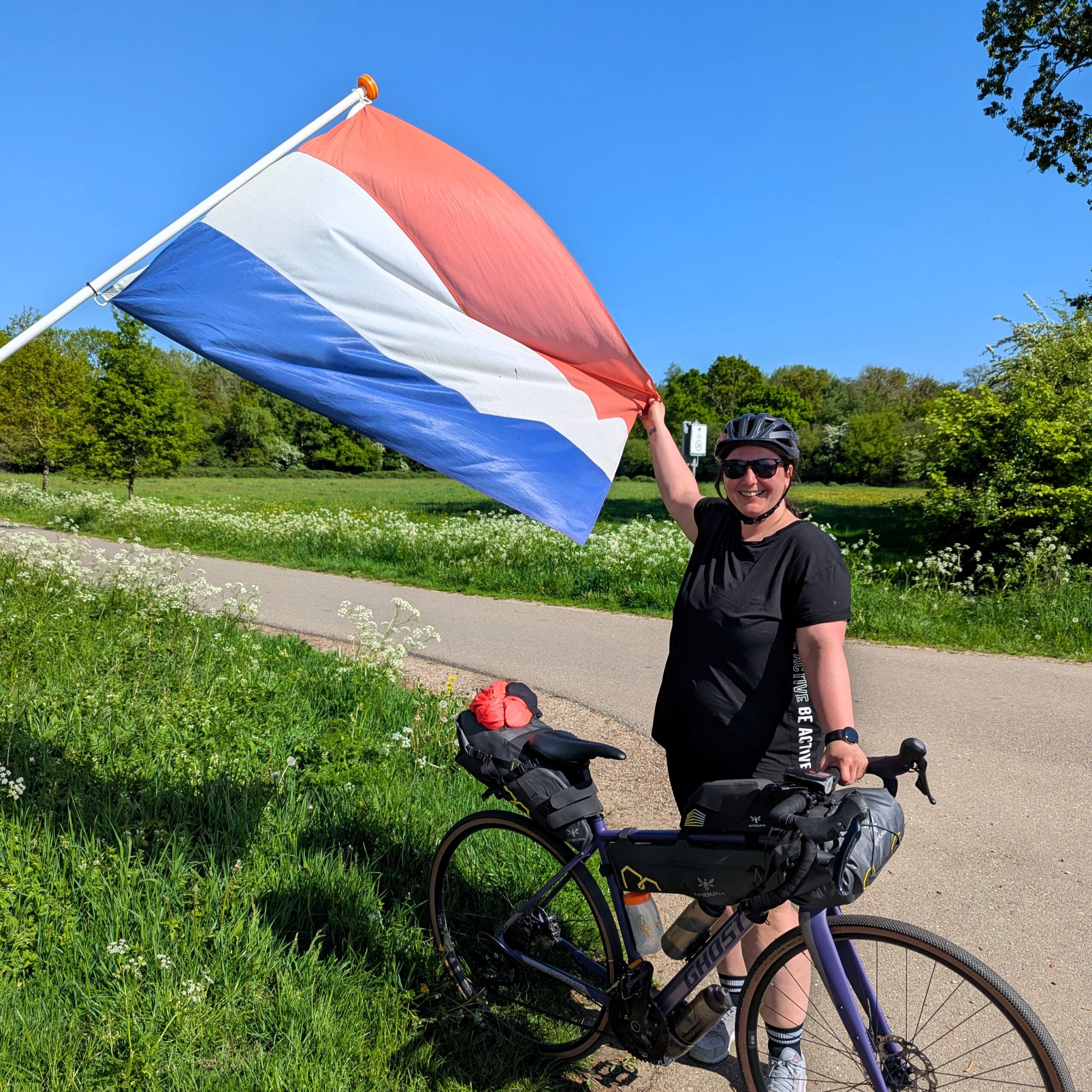 Frau mit auf Fahrradreise auf Maas- Radweg mit Niederlande Flagge