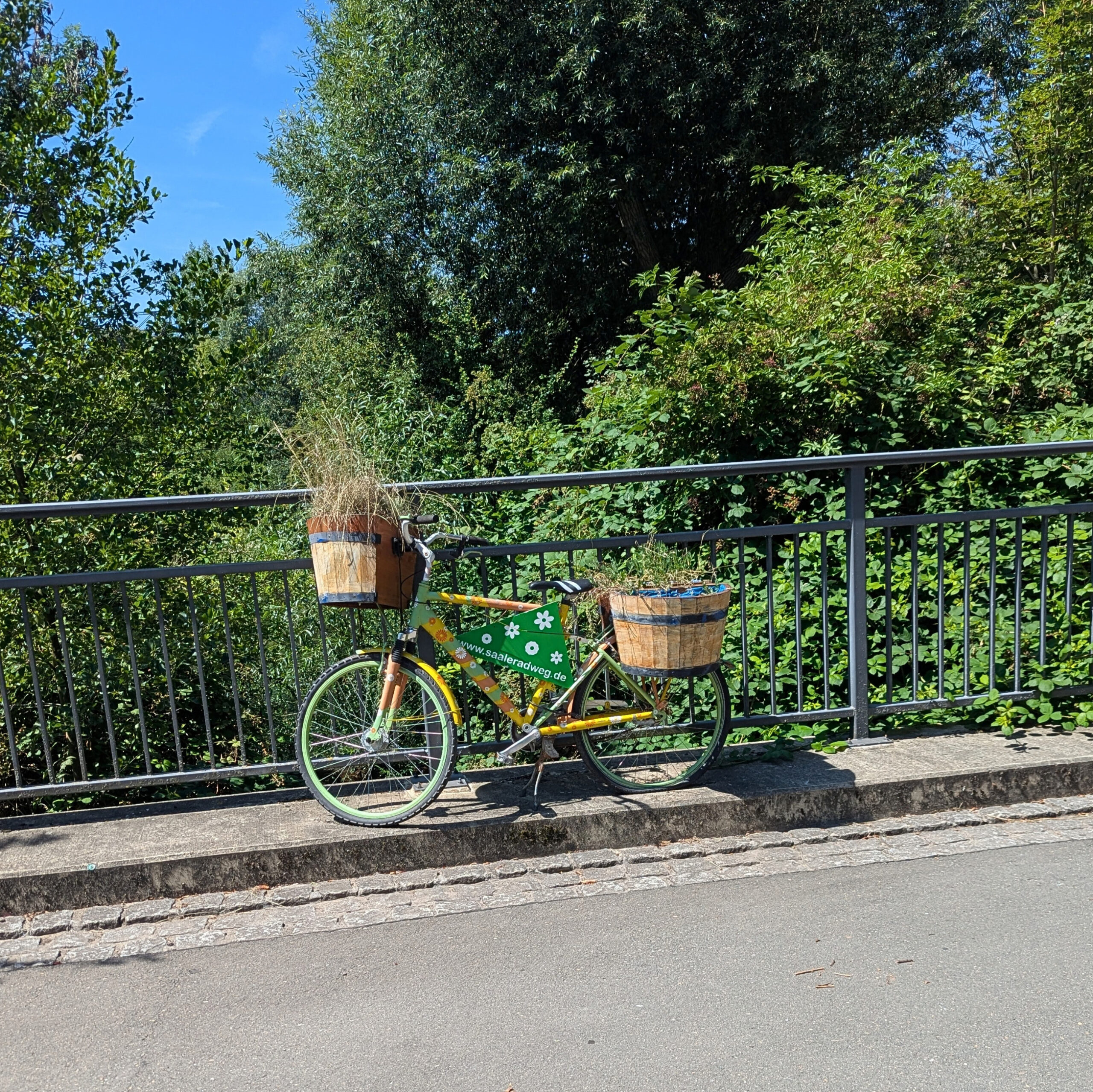 Fahrrad an Brücke geschmückt mit Blumen und Touristeninformationen zum Saaleradweg